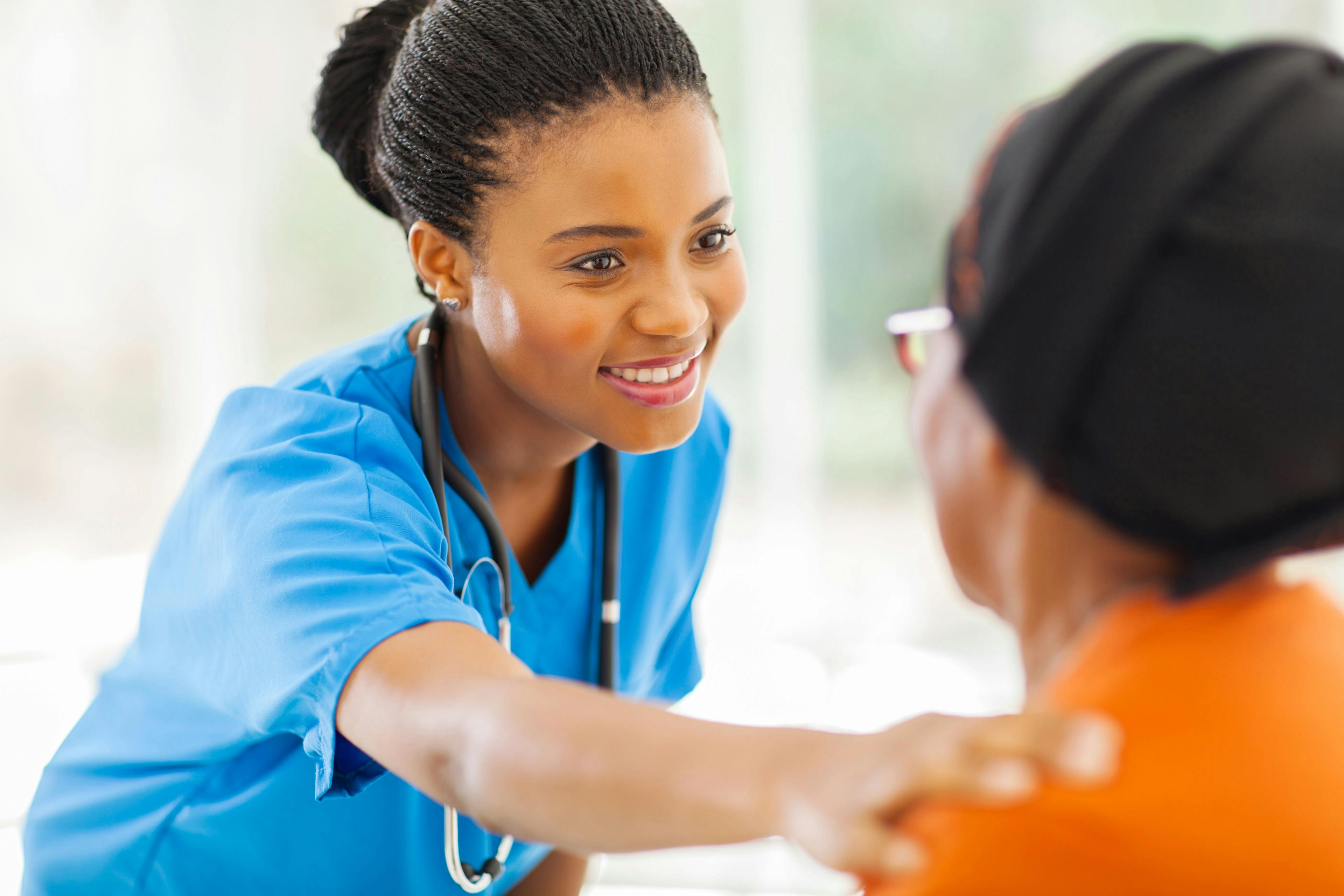A Black health care provider touches the shoulder of a Black woman patient.