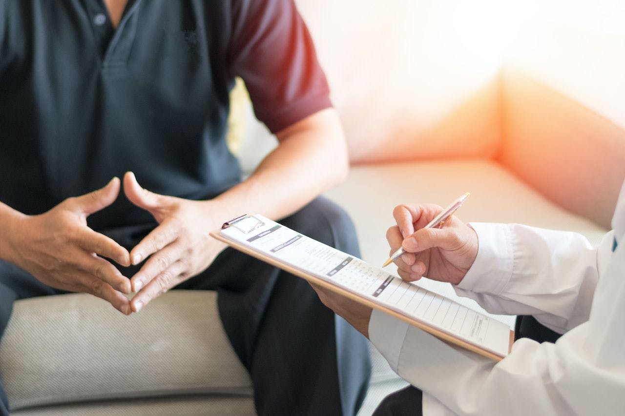 doctor writing on clipboard while talking to patient