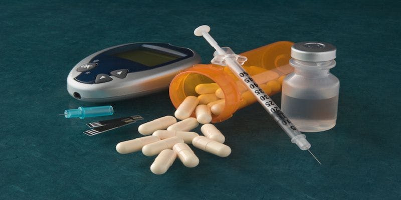 vial of insulin, syringe, bottle of pills, and a blood sugar reader laying in a pile